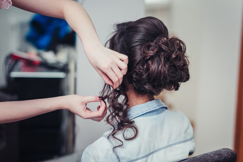curly brunette hair in an updo and hands fixing the curls