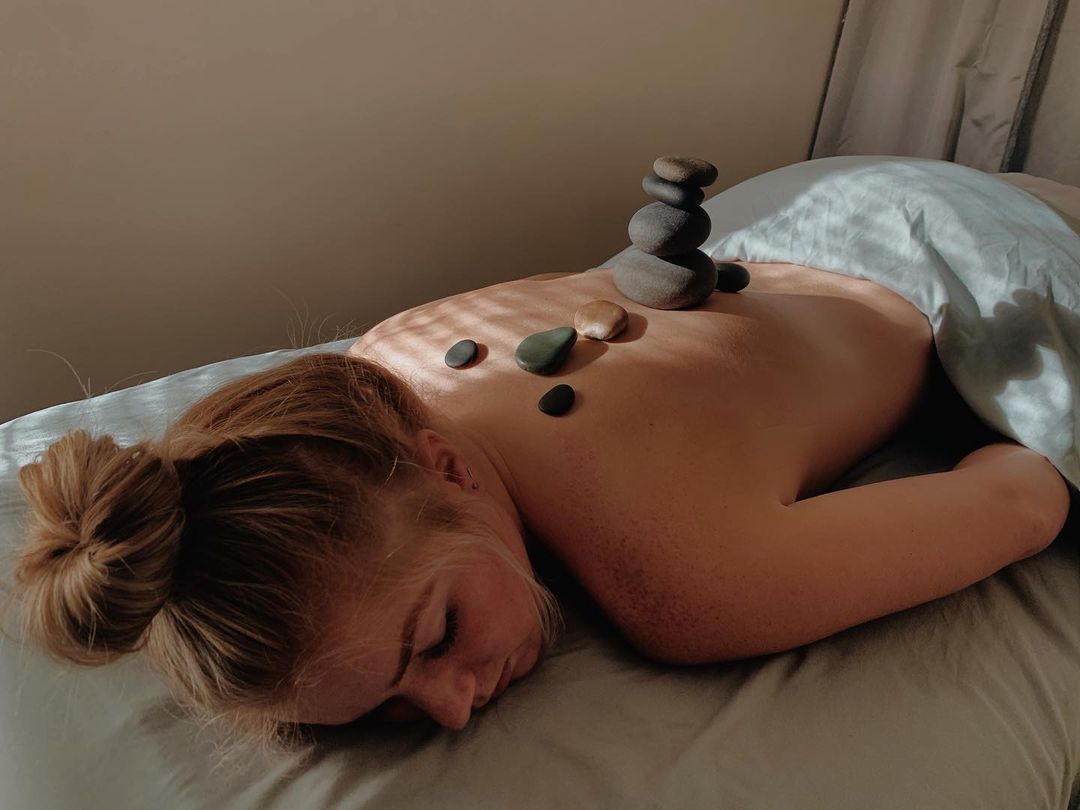 Client receives hot stone massage therapy treatment on back while lying on massage table