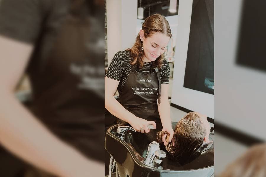 licensed cosmetologist washing hair at a sink in salon