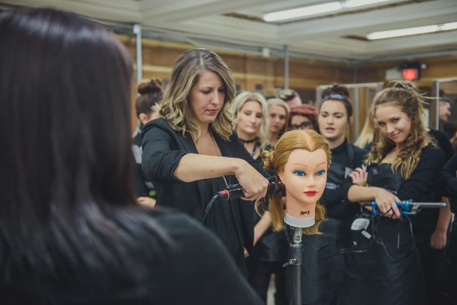 Cosmetology instructor and students dressed-in black working on model head of hair
