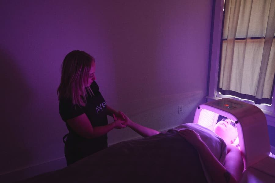 aveda graduate provides facial treatment in a softly lit room with purple lighting