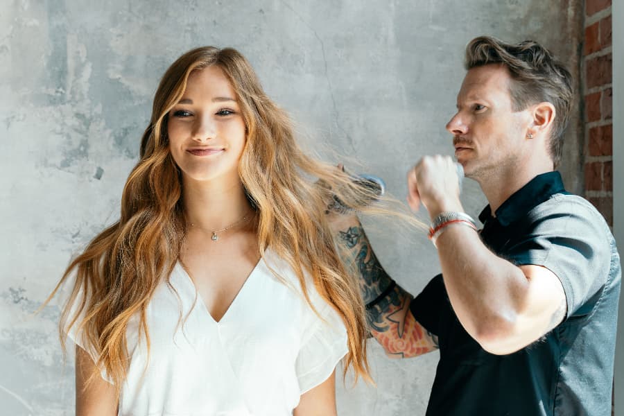 hairstylist from Aveda Institutes in Arizona styles a young woman's long wavy hair
