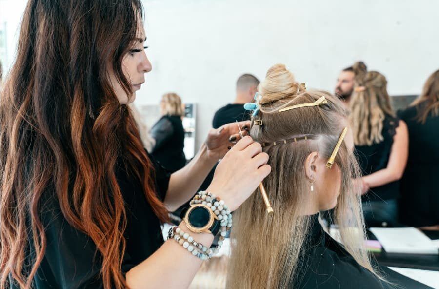 hairstylist trained at a beauty school attaches hair extensions