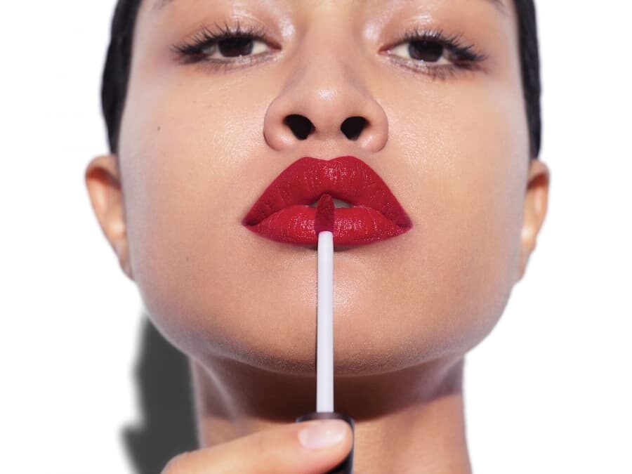 close up of a Aveda model applying vibrant red liquid lipstick