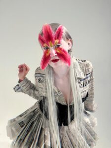 aveda model in denver poses with flower petals on face and newspaper dress